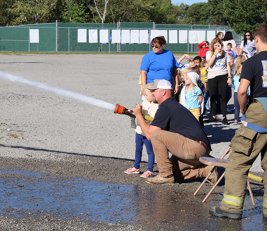 Fire Fighter Andrew Russell helps students with the fire hose