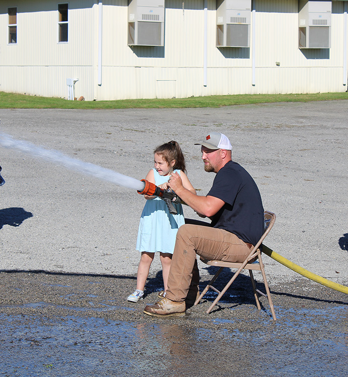 Fire Fighter Andrew Russell helps students with the fire hose