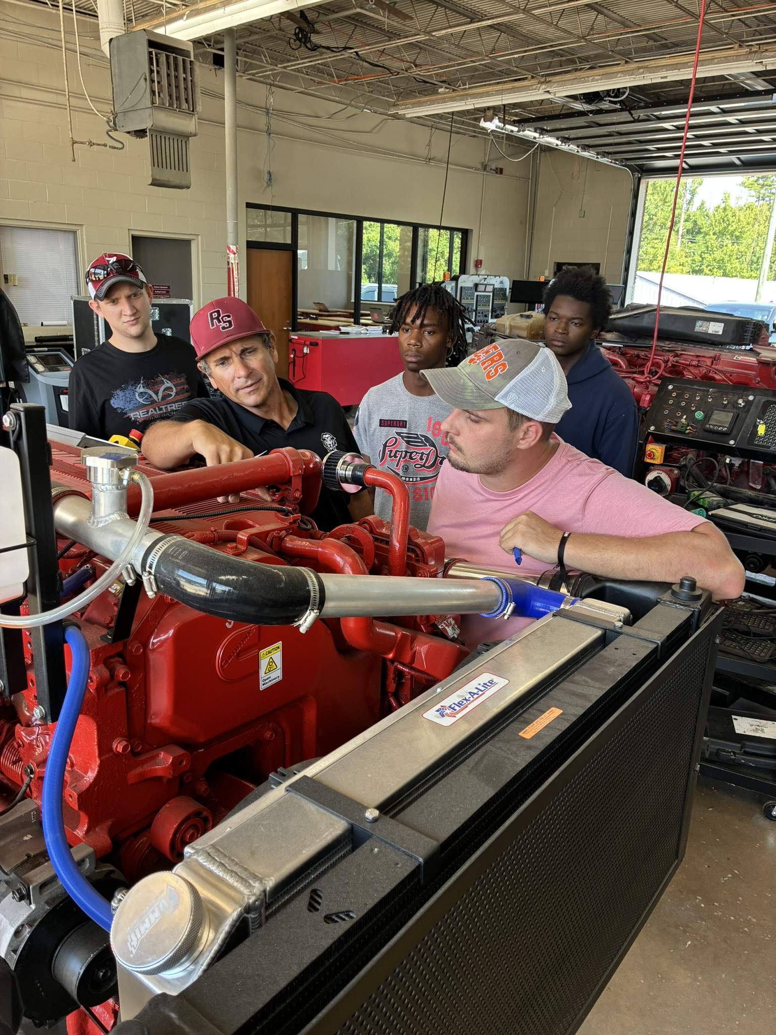 A group of students listens as a diesel technology instructor discusses around a diesel engine