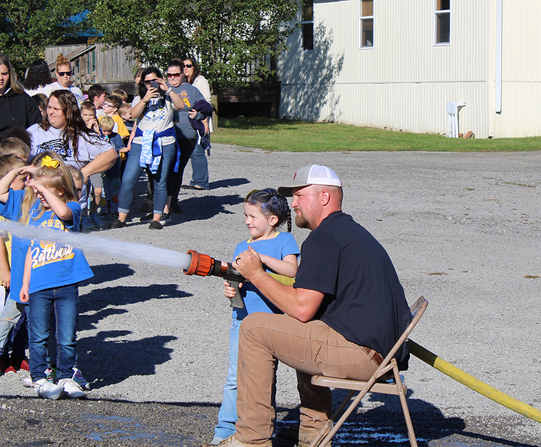 Fire Fighter Andrew Russell helps students with the fire hose