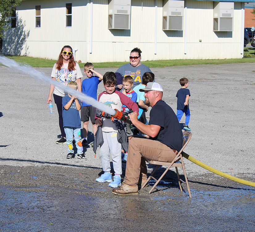 Fire Fighter Andrew Russell helps students with the fire hose