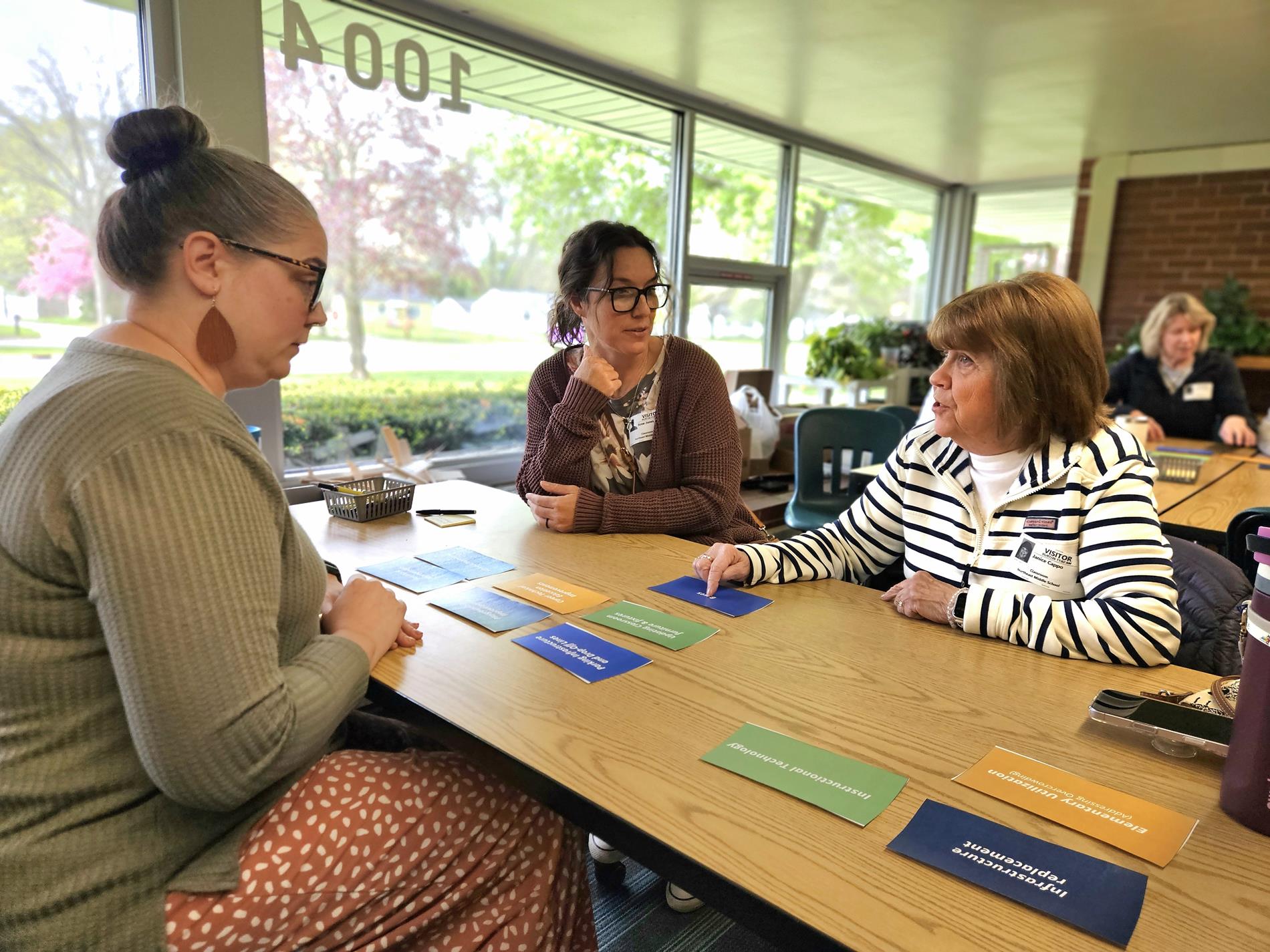 Three women sit at a table discussing key priorities for the facility planning process