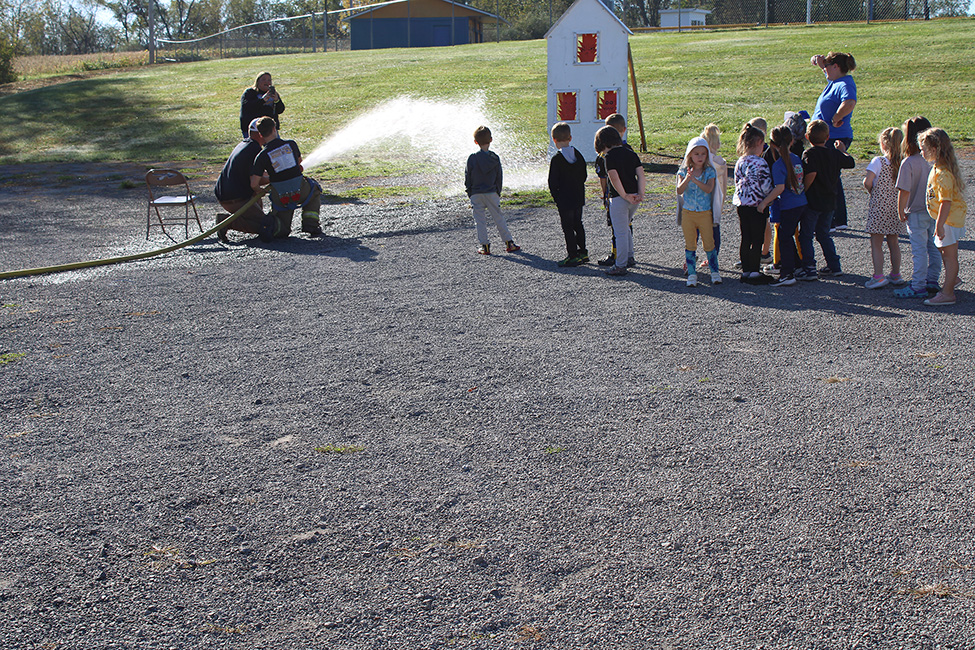 Fire Fighter Andrew Russell helps students with the fire hose