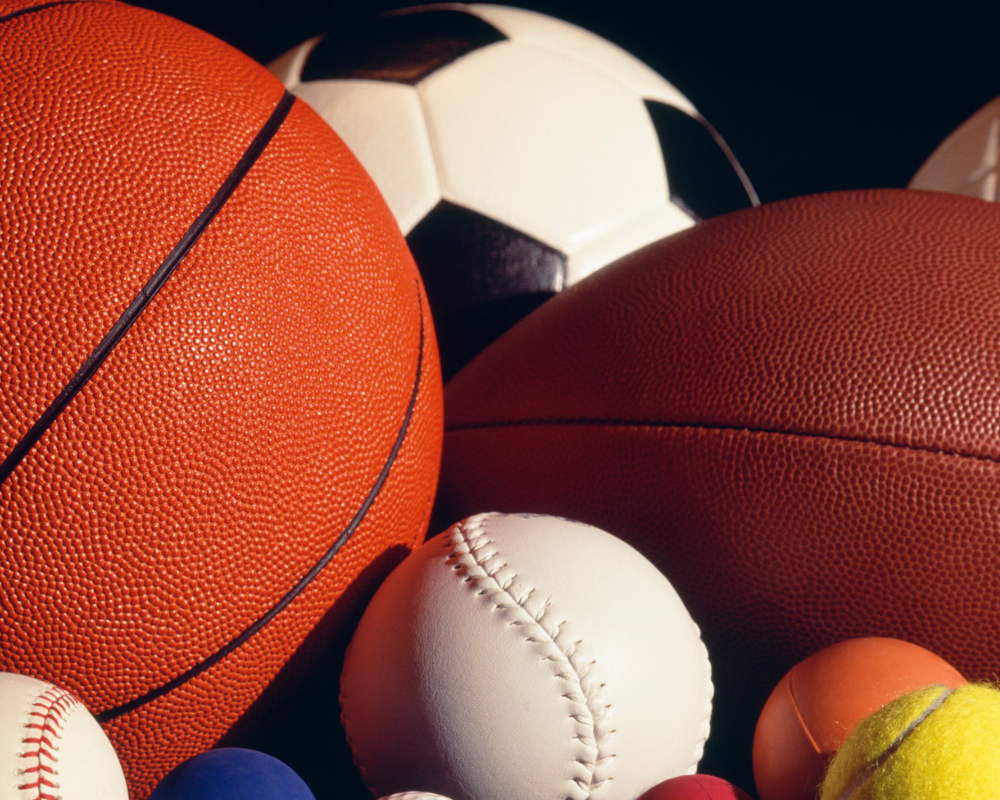 A basketball, football, soccer ball, baseball, softball, tennis ball, and racquet balls sit together
