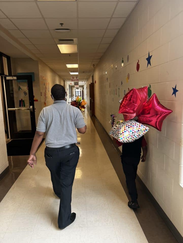 Mr. Davis and a student surprising Ms. Ellis with flowers and balloons. 