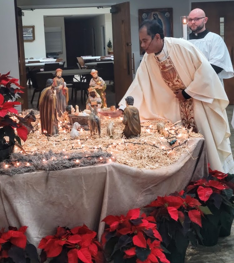 Father Antony places the Baby Jesus in the Nativity scene on Christmas Eve assisted by Seminarian Ross Gilliland