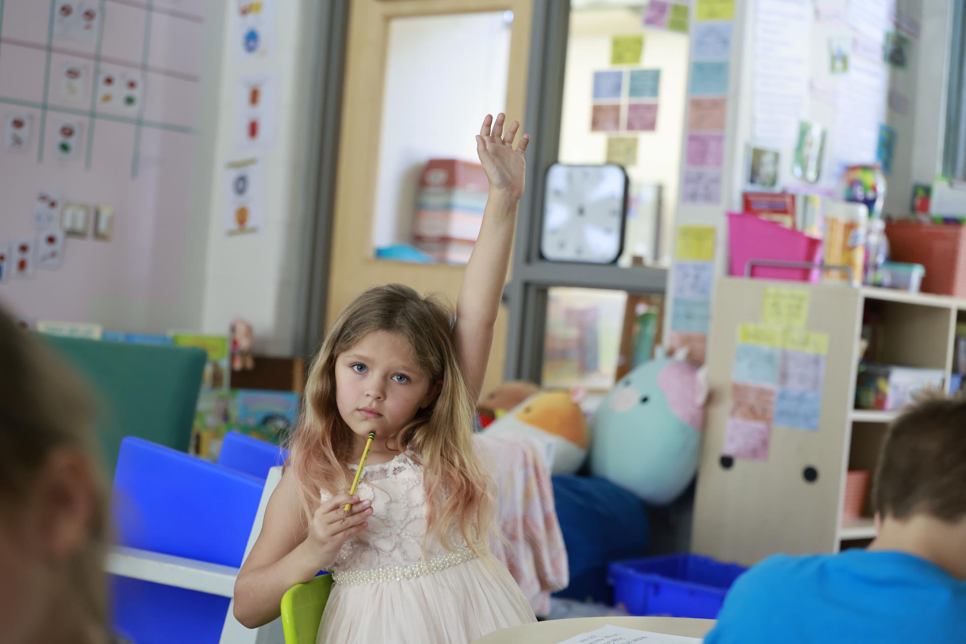 Elementary student raising her hand sitting at desk in classroom