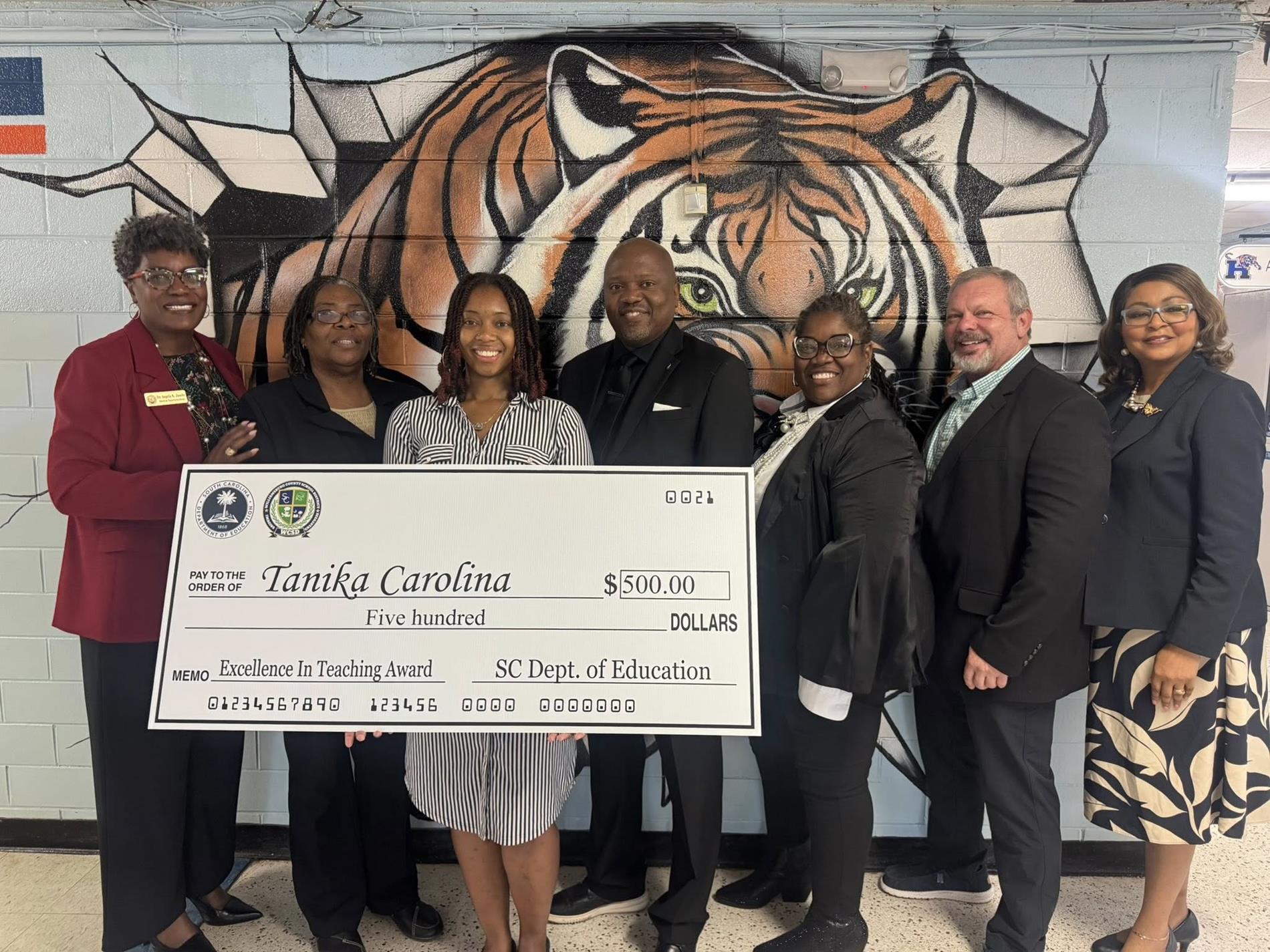 people standing in hallway holding large check 