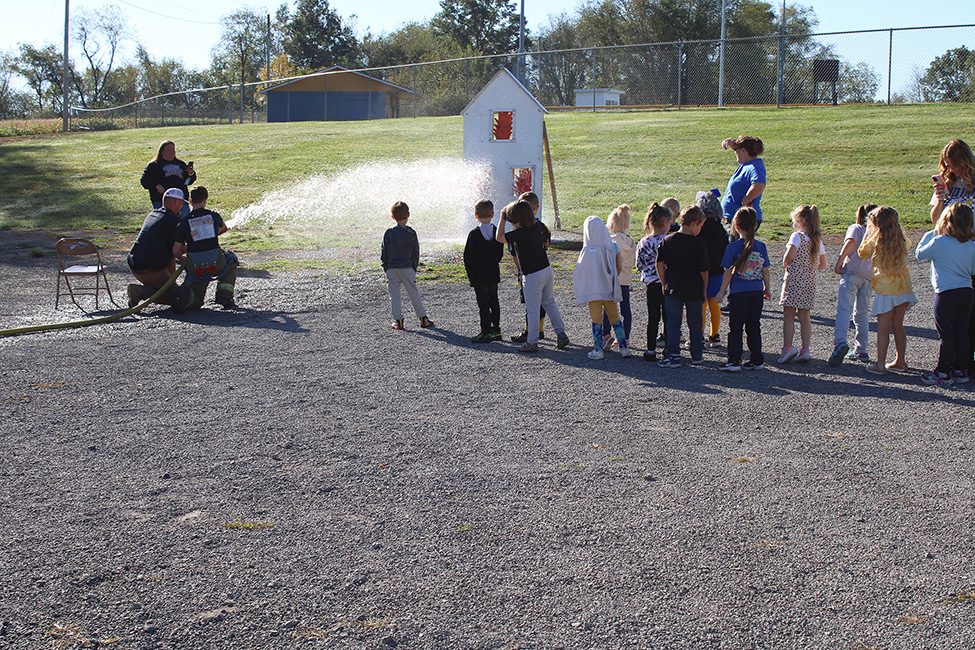 Fire Fighter Andrew Russell helps students with the fire hose