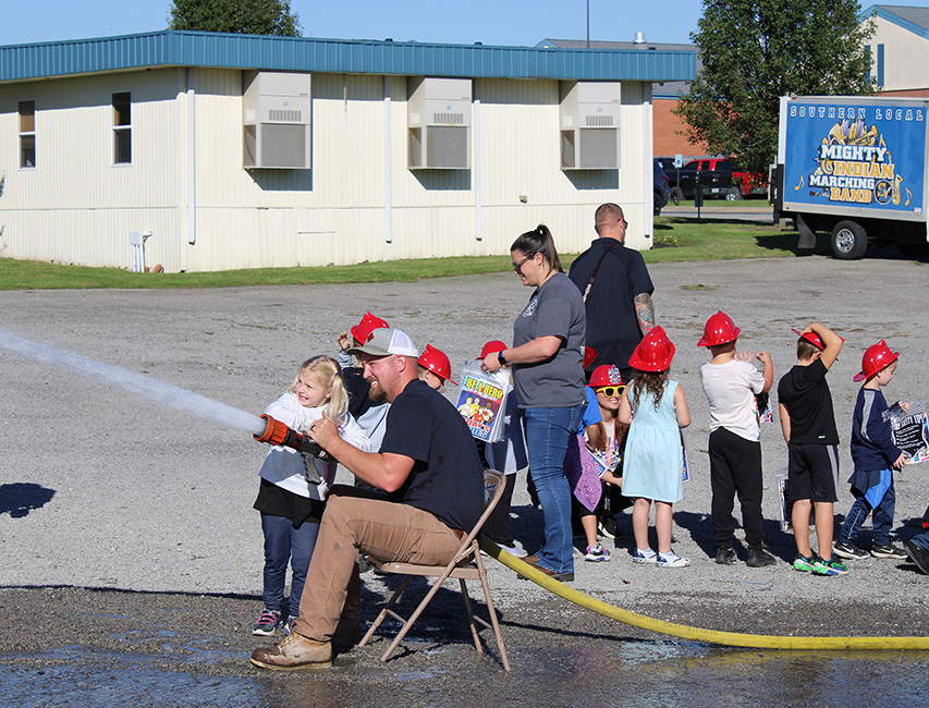 Fire Fighter Andrew Russell helps students with the fire hose