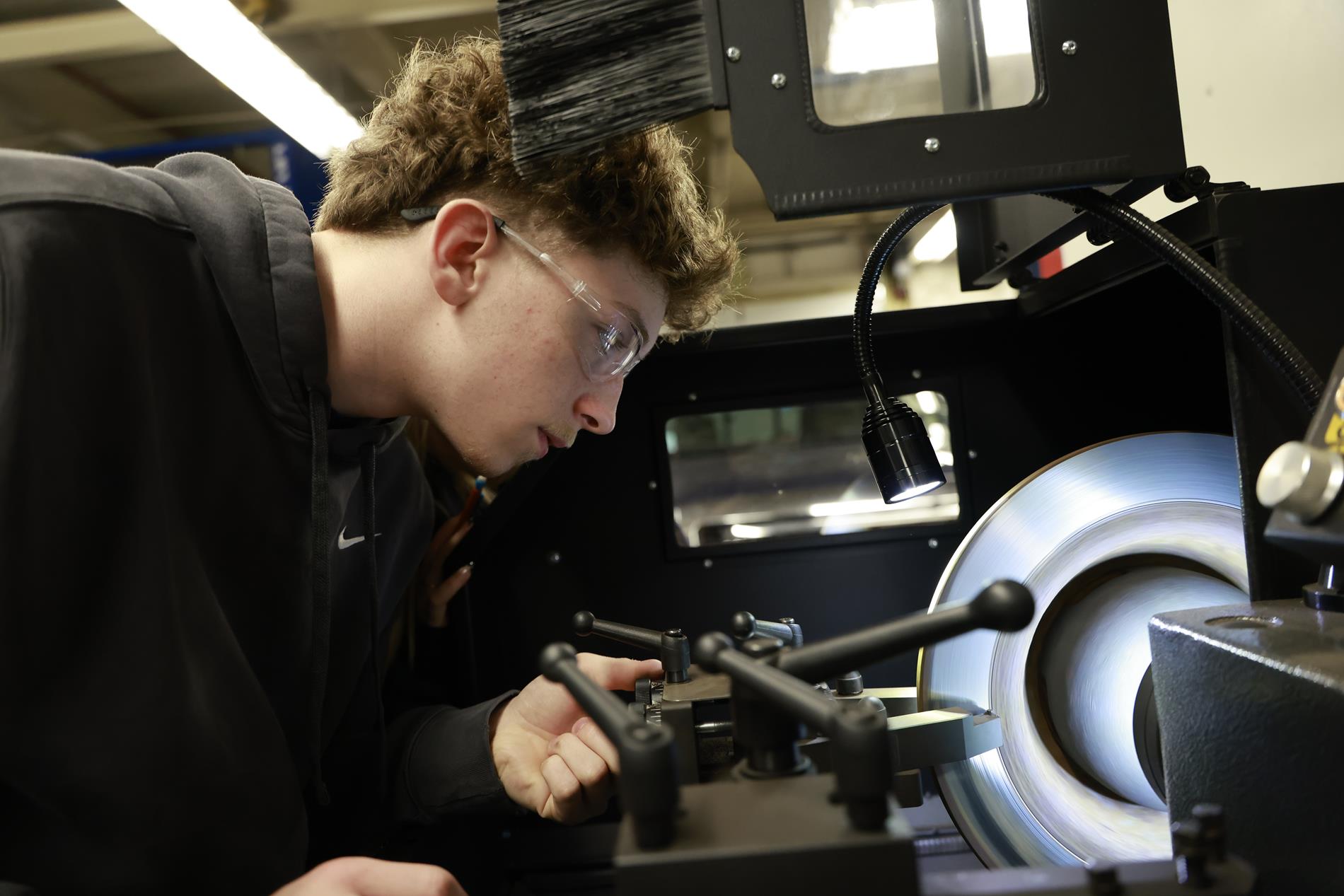 A high school boy runs a part through a machine at the Auto Tech lab