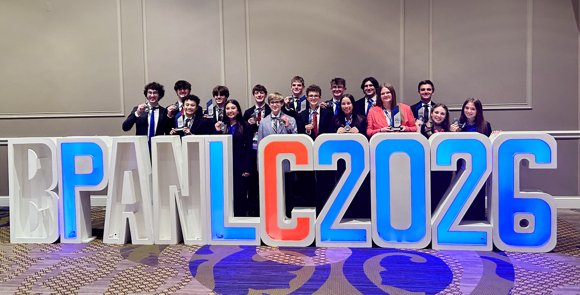 All MHS BPA students who received medals holding their hardware in front of a giant BPA NLC art installation