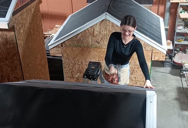 A female student nailing shingles to a shed roof in construction class.