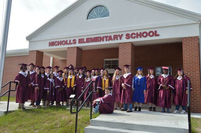 Former graduates of Nicholls Elementary School standing in front of the new school building in their caps and gowns