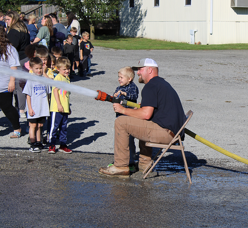 Fire Fighter Andrew Russell helps students with the fire hose