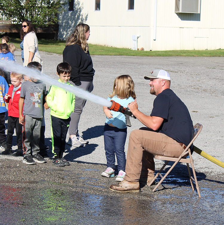 Fire Fighter Andrew Russell helps students with the fire hose