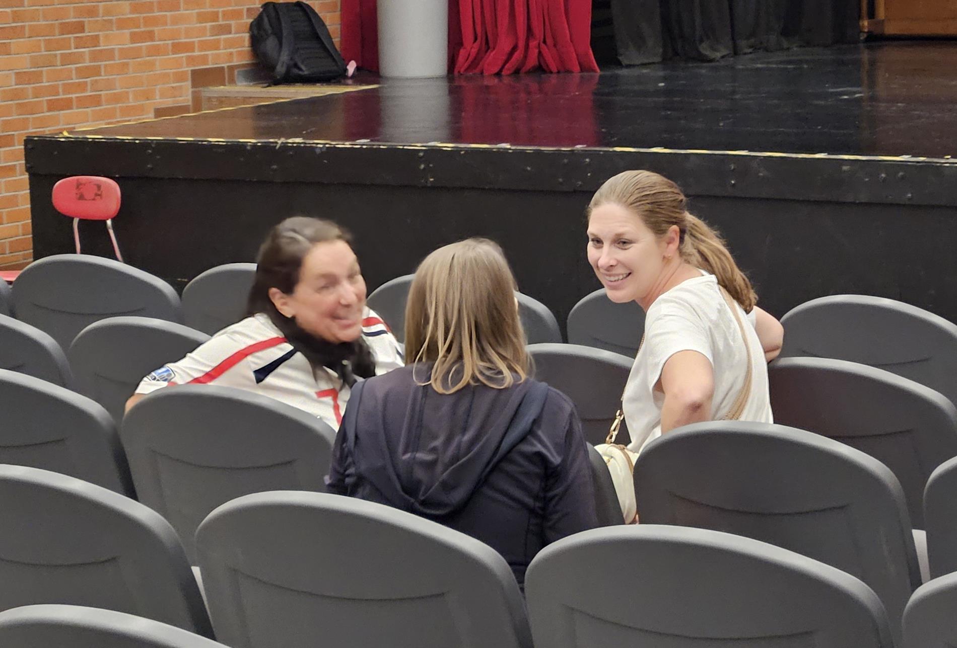 Three women sit together in auditorium chairs and talk about the presentation