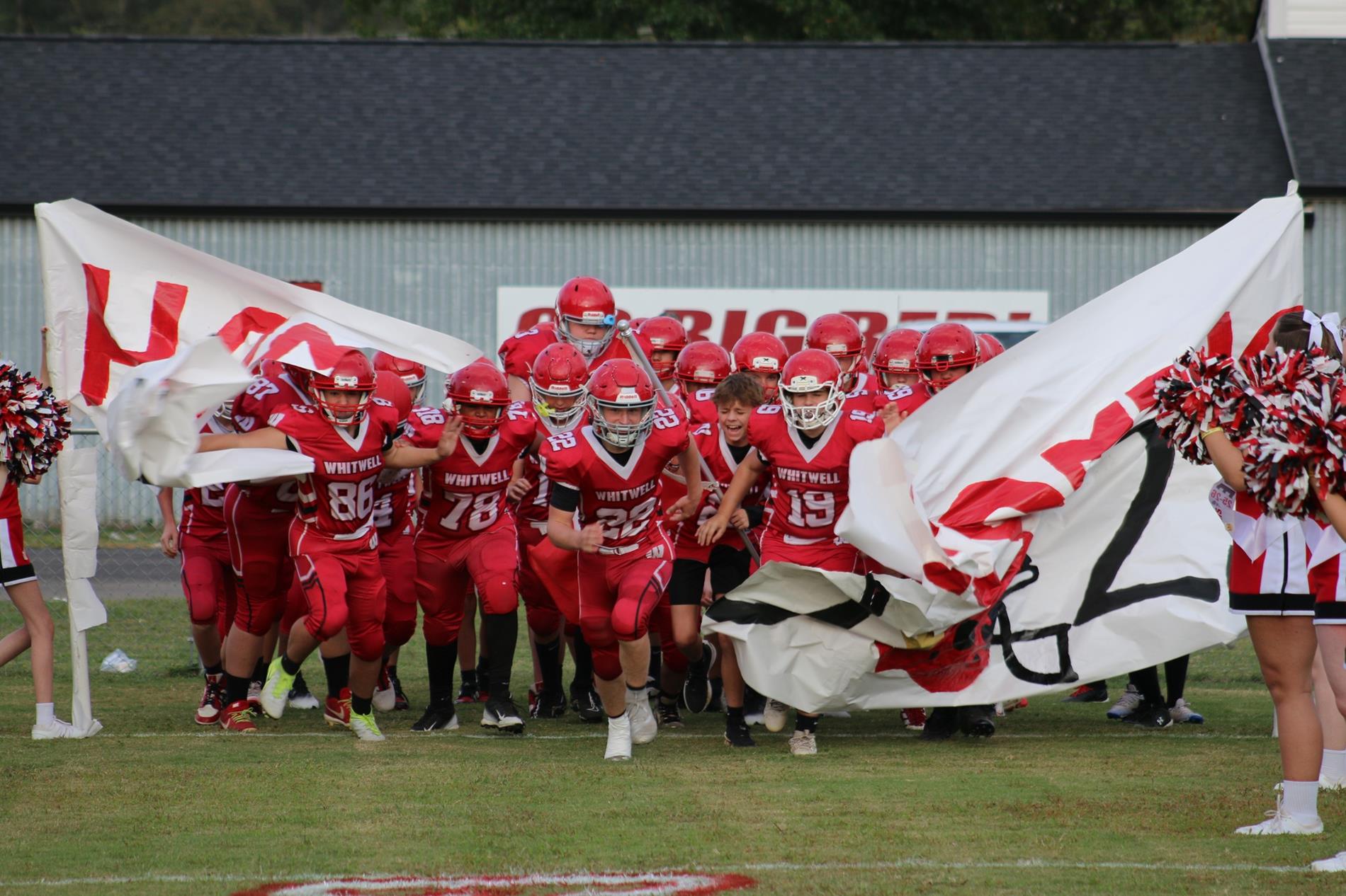 WMS football team running through HOCO '25 sign with cheerleader spirit line.