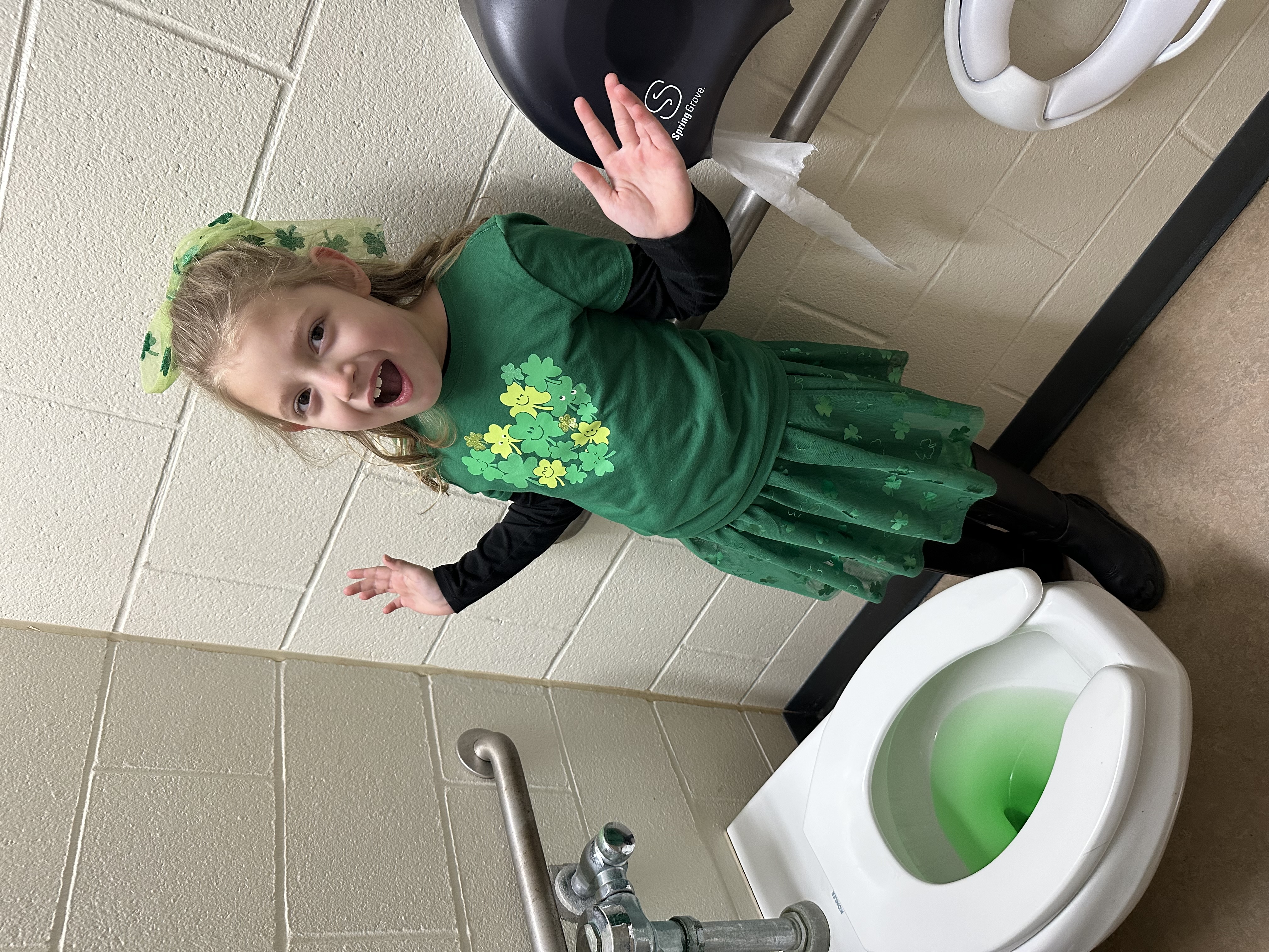 student standing next to a toilet with green "pee" left by the leprechaun. 