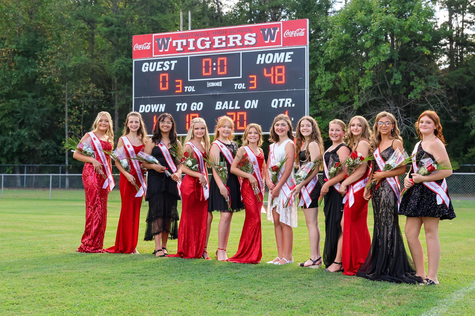 Girls on the homecoming court in red, black and white dresses with red rose bouquets