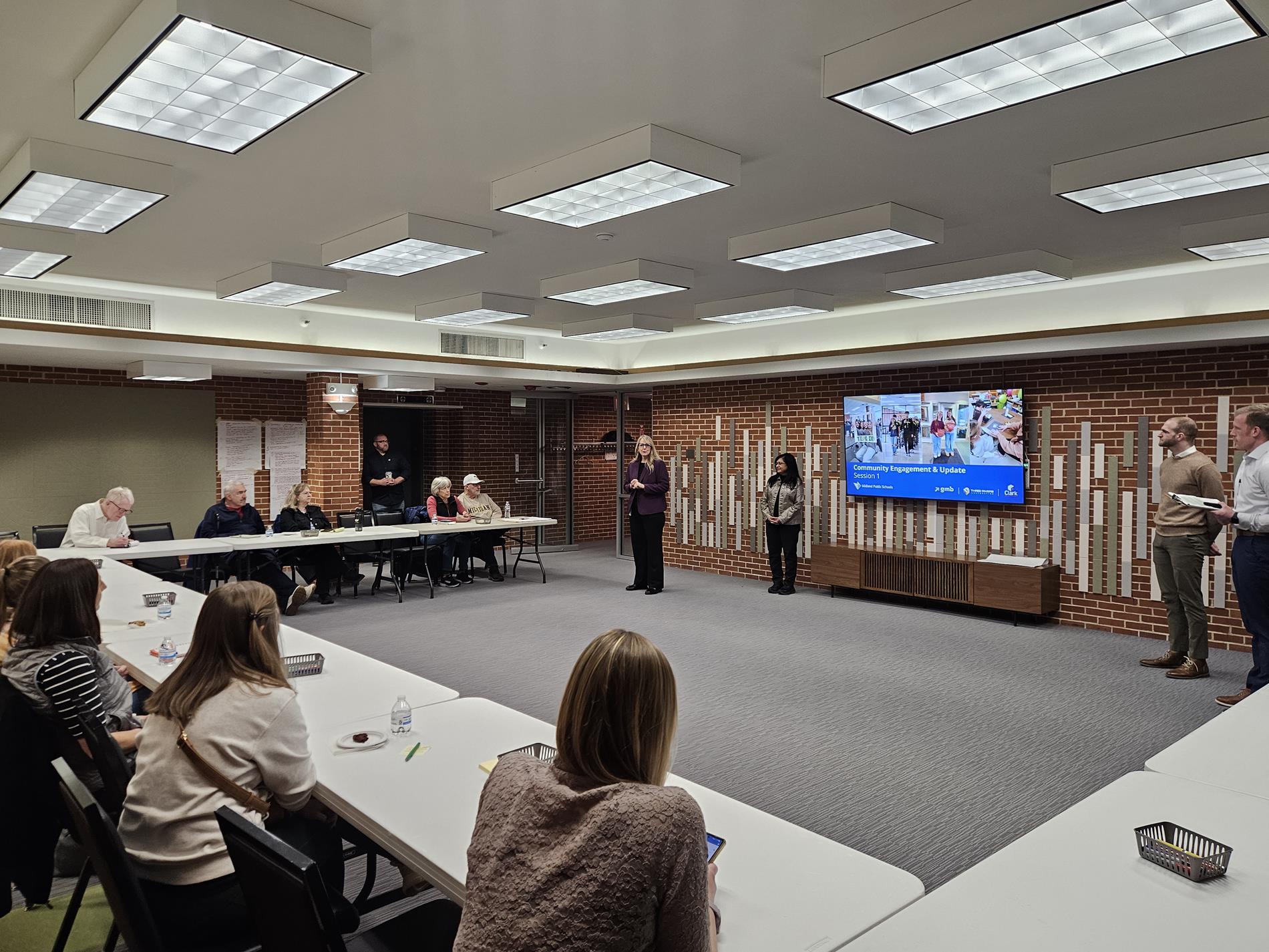 A group of residents engage in conversation during a facility planning presentation at the Library Community Room
