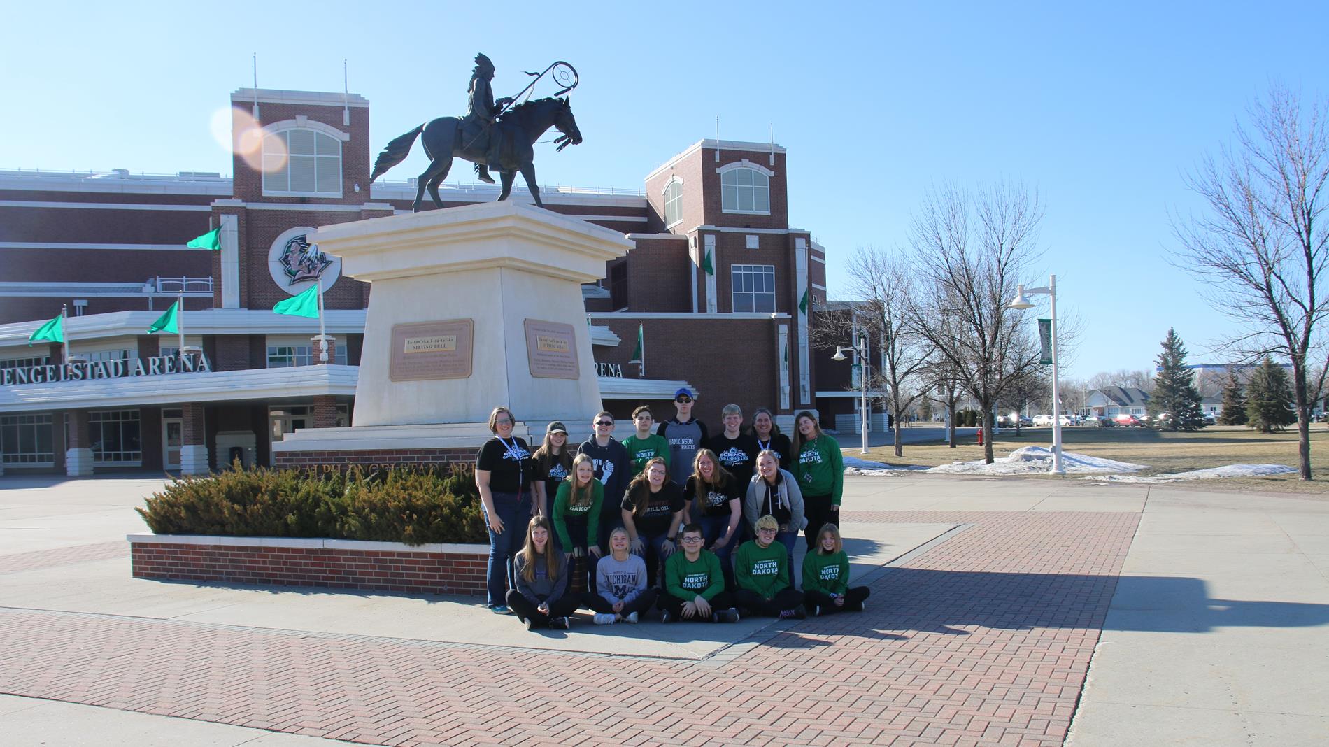 Science fair students posing under a statue at Ralph Engelstad Arena in Grand Forks