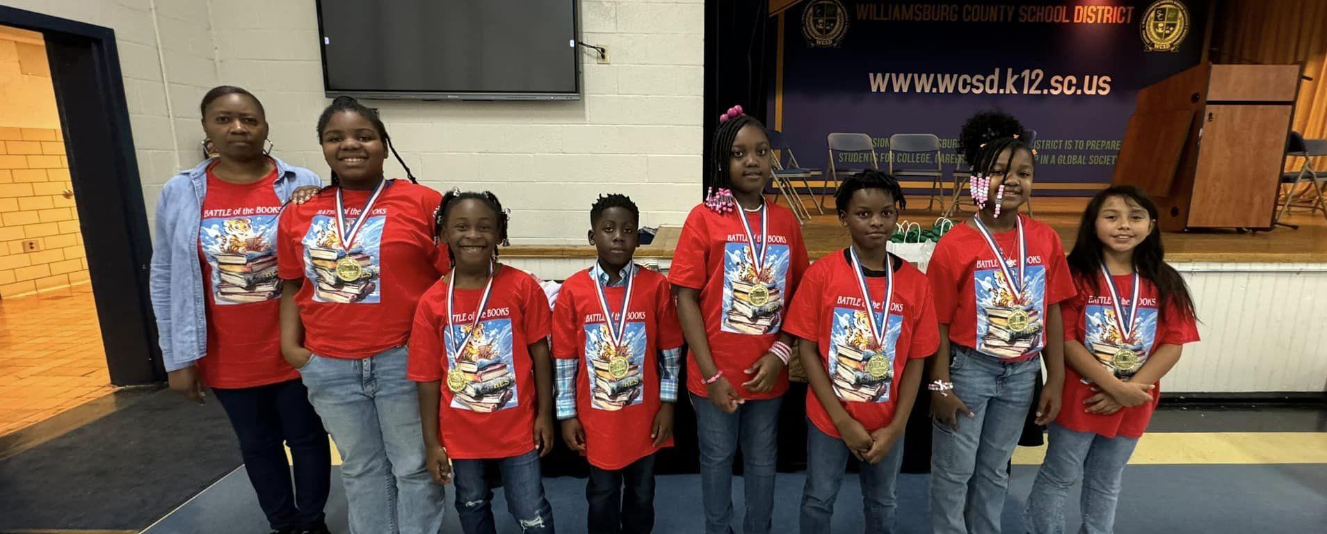 students standing in line in front of stage wearing their award medals at Battle of the Books 