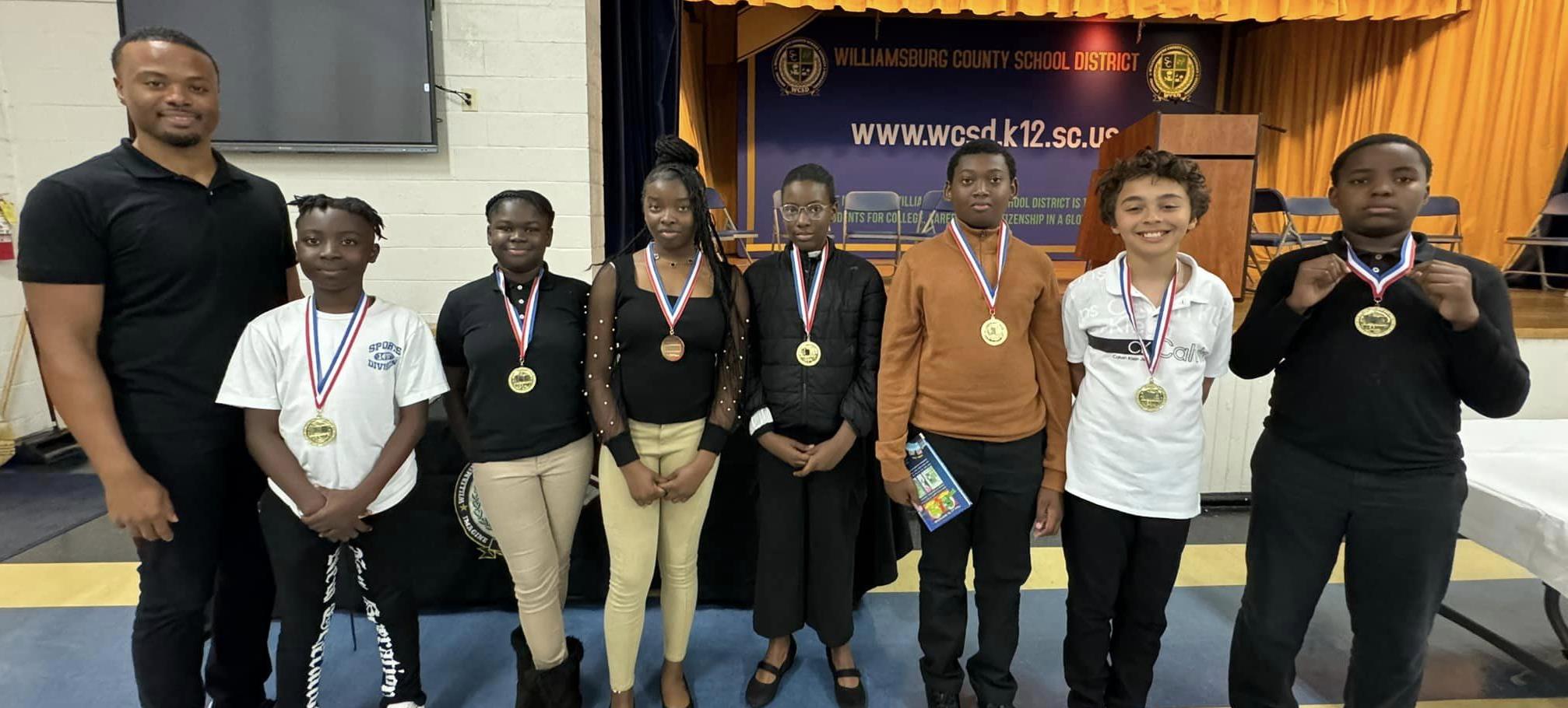 students standing with adult wearing award medals