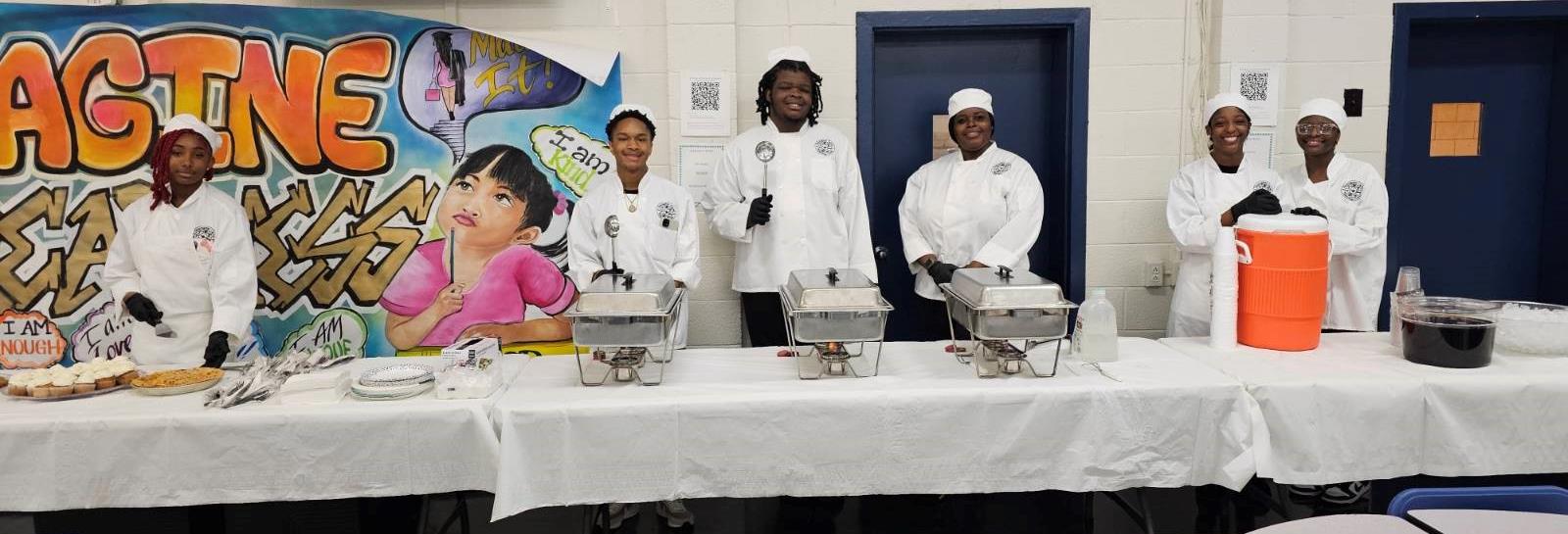 culinary students standing behind table with serving pans on them