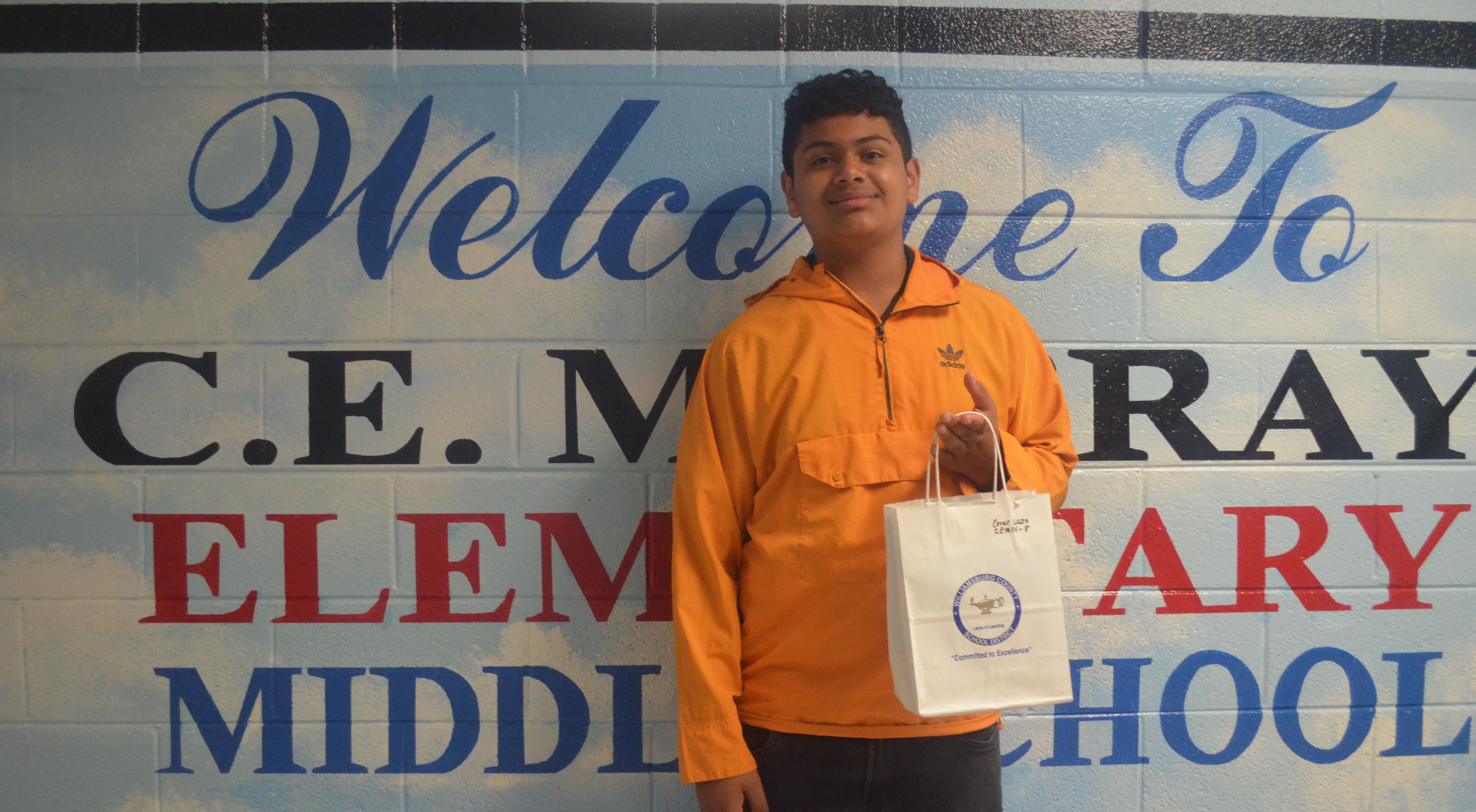 welcome to c.e. murray elementary middle school. student standing in front of wall mural holding gift bag