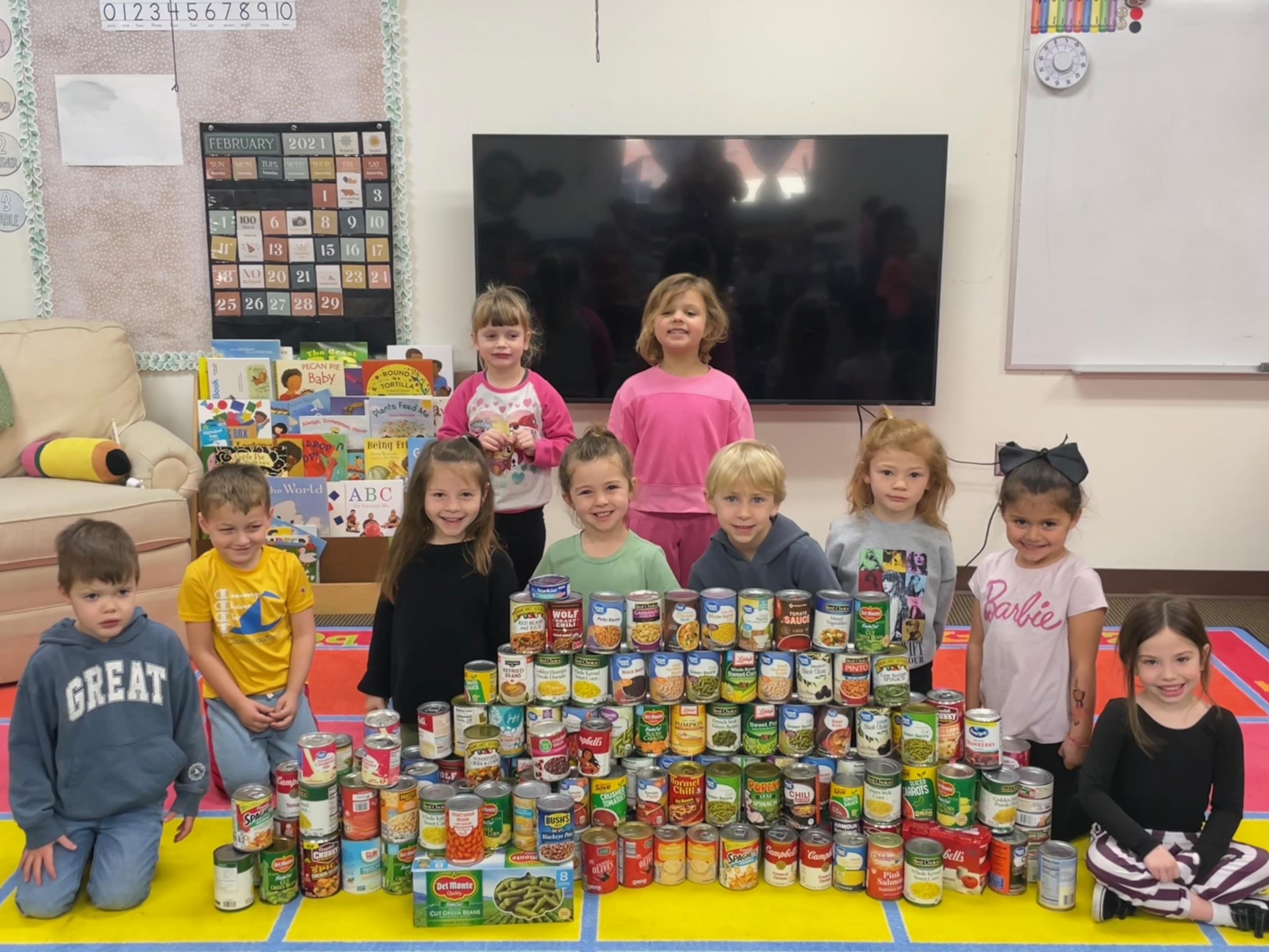 Ten pre-k students pose with 100 cans of food. 