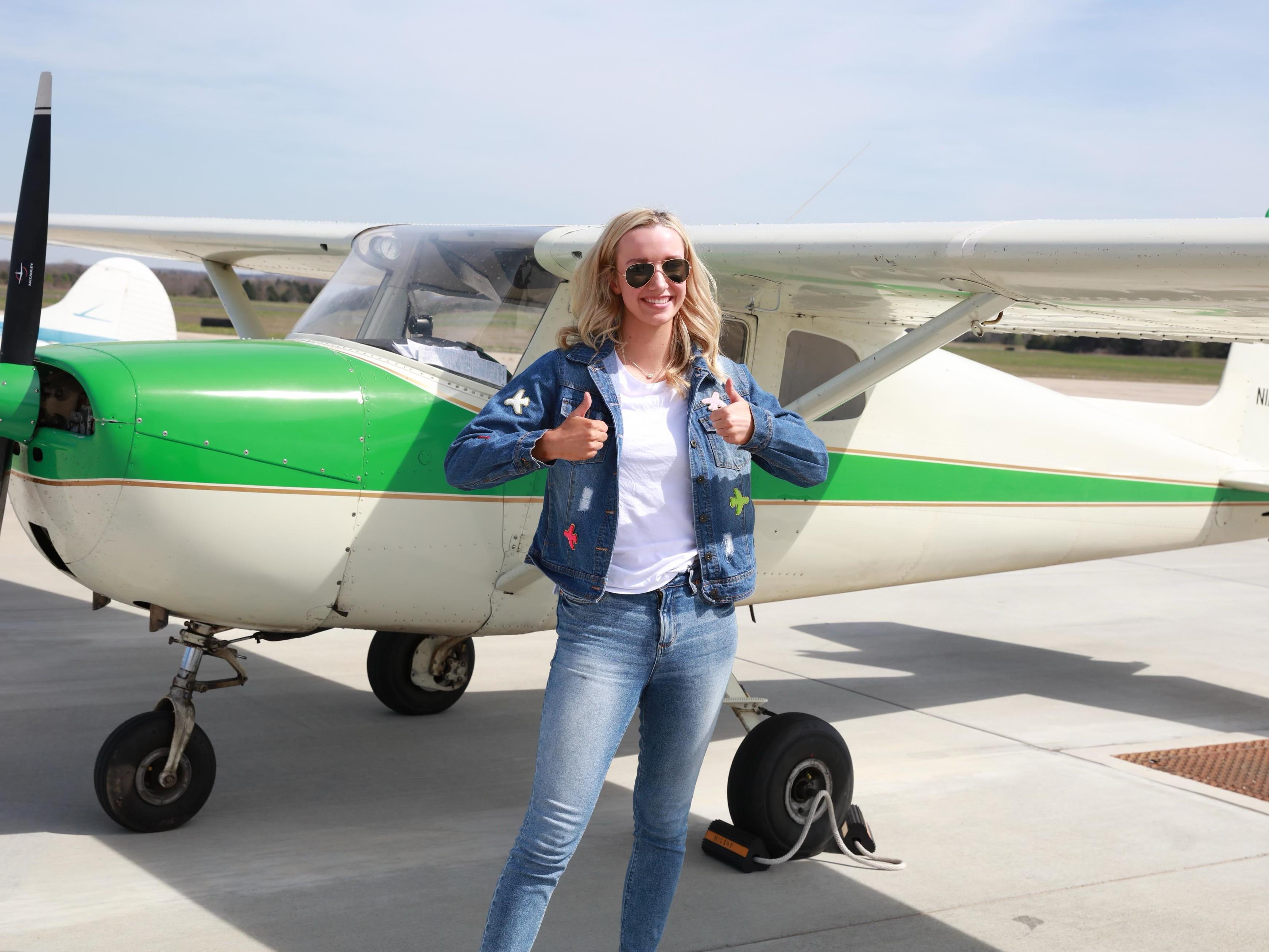 Ava Manwell stands by a green and white airplane holding two thumbs up.