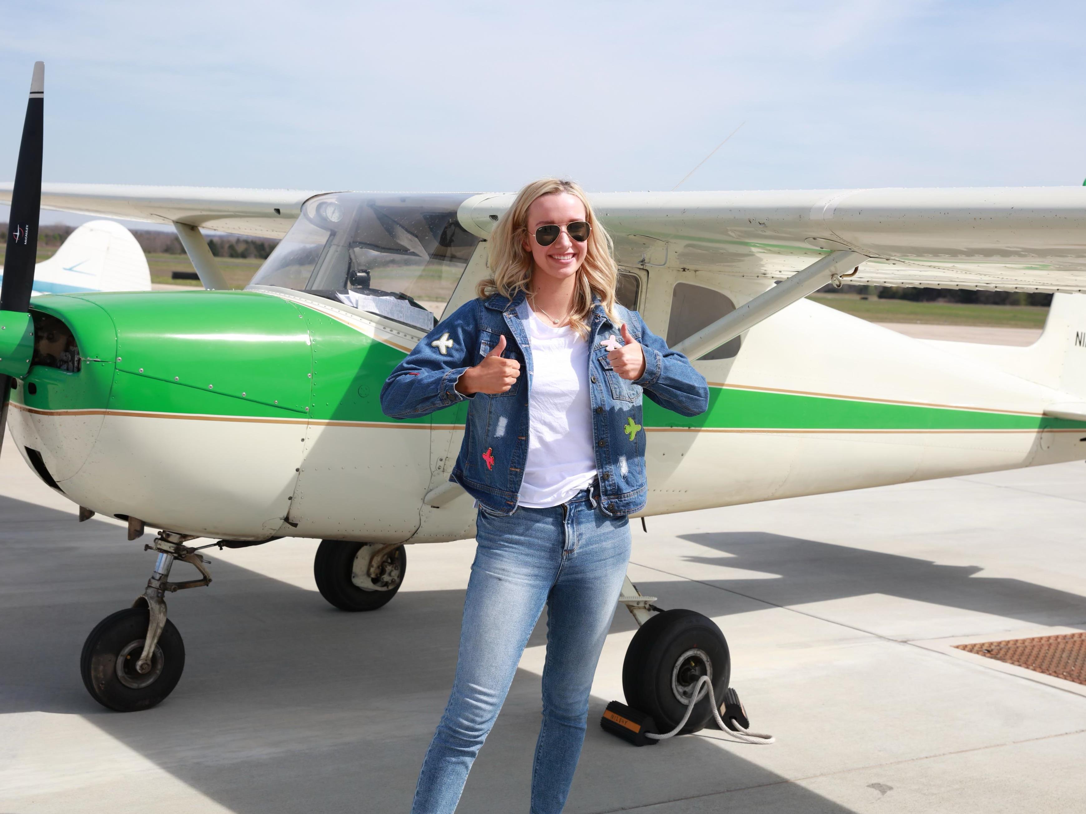 Ava Manwell stands by a green and white airplane holding two thumbs up. 