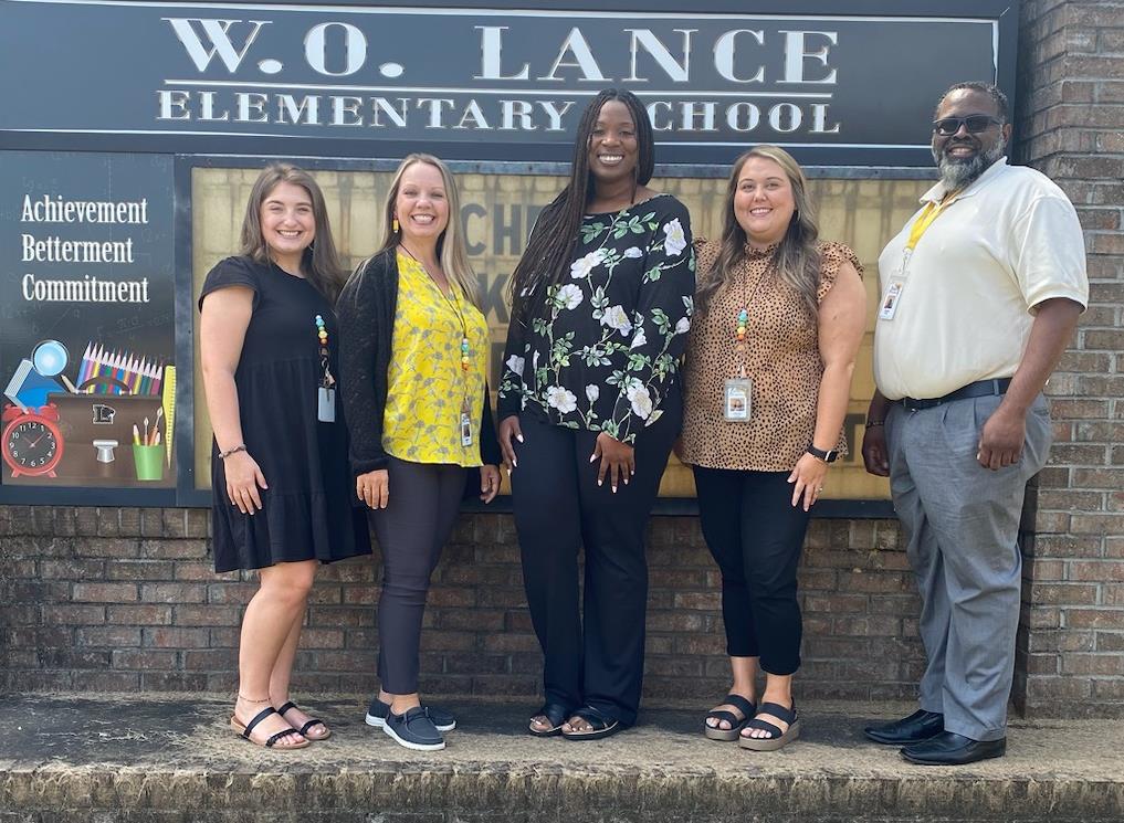 Lance's Office Staff standing in front of the school sign. From left to right, Kira Morgan, Donna Bell, Reagan Gilbert, Crystal Autry, and Wilfred Dunn
