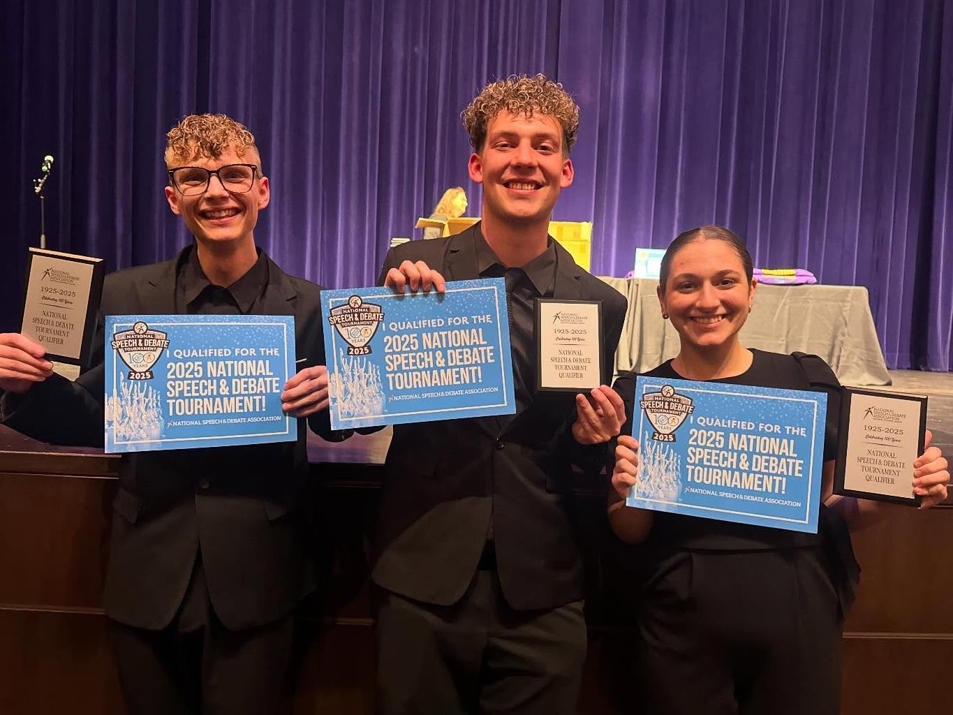 Three students hold certificates stating they will compete in the National Speech and Debate Tournament.