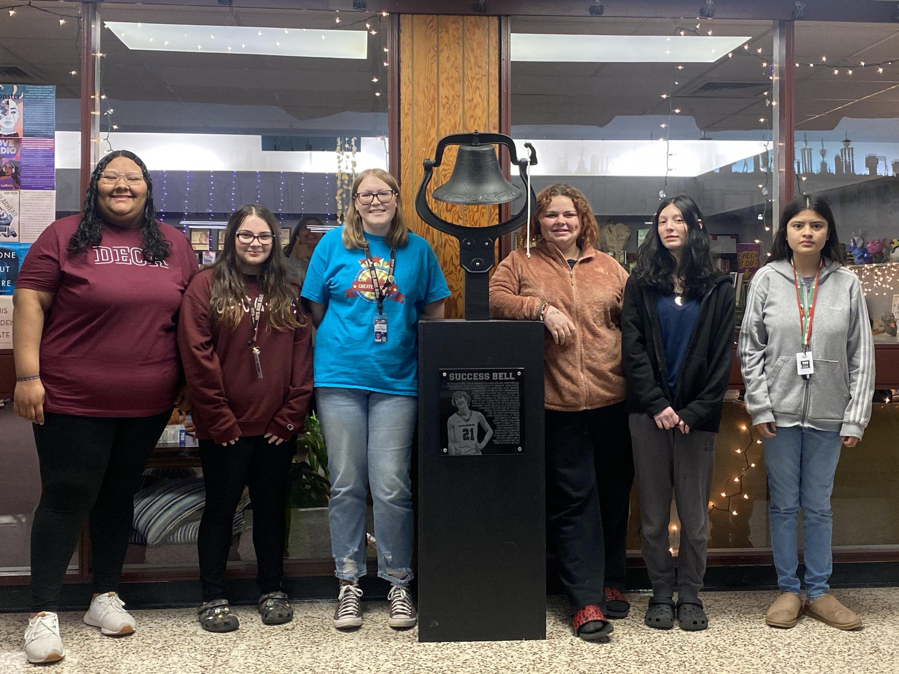 yearbook students pose with the success bell at Ada High School.