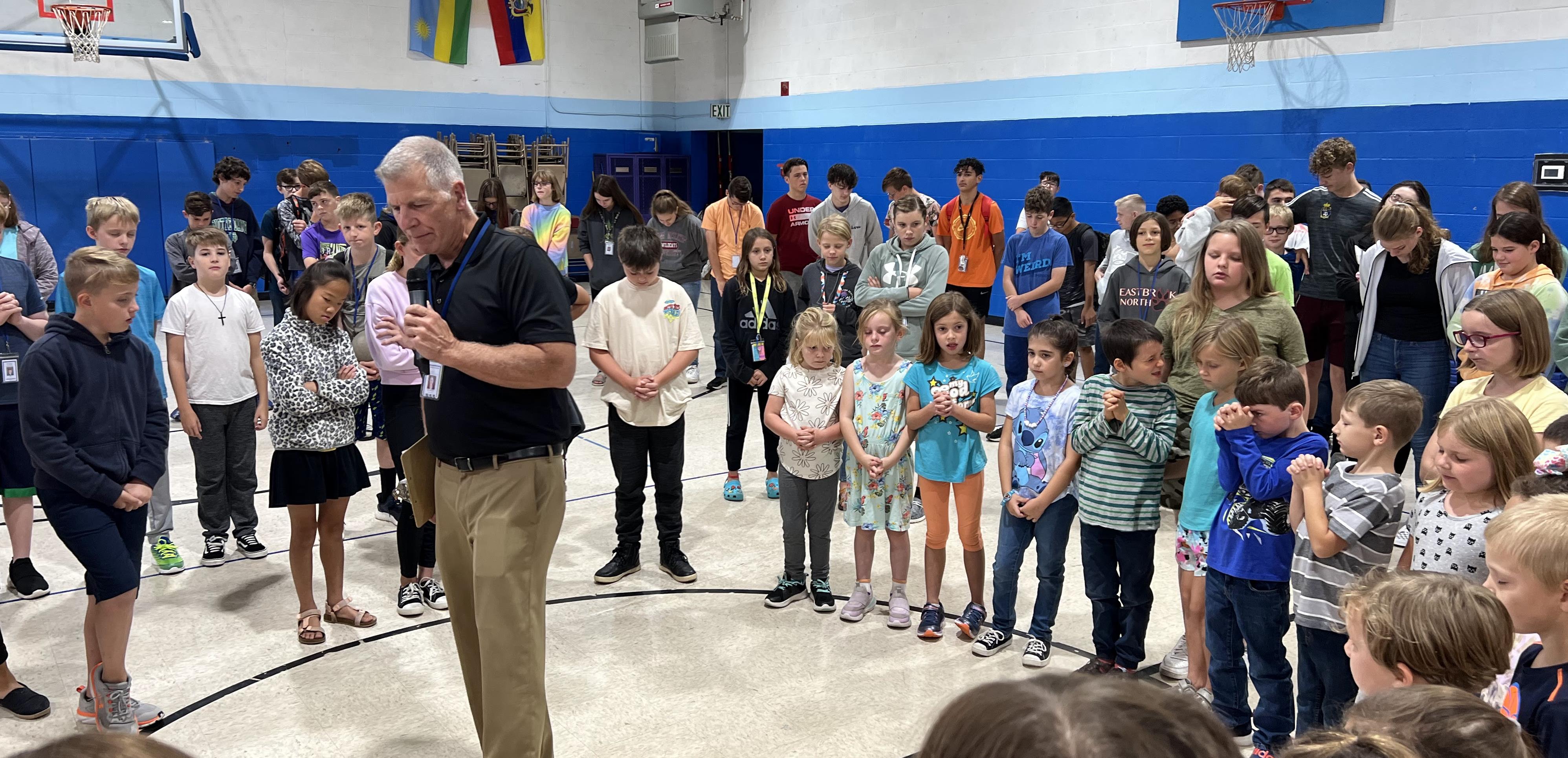 kids gathered in a circle around a man speaking