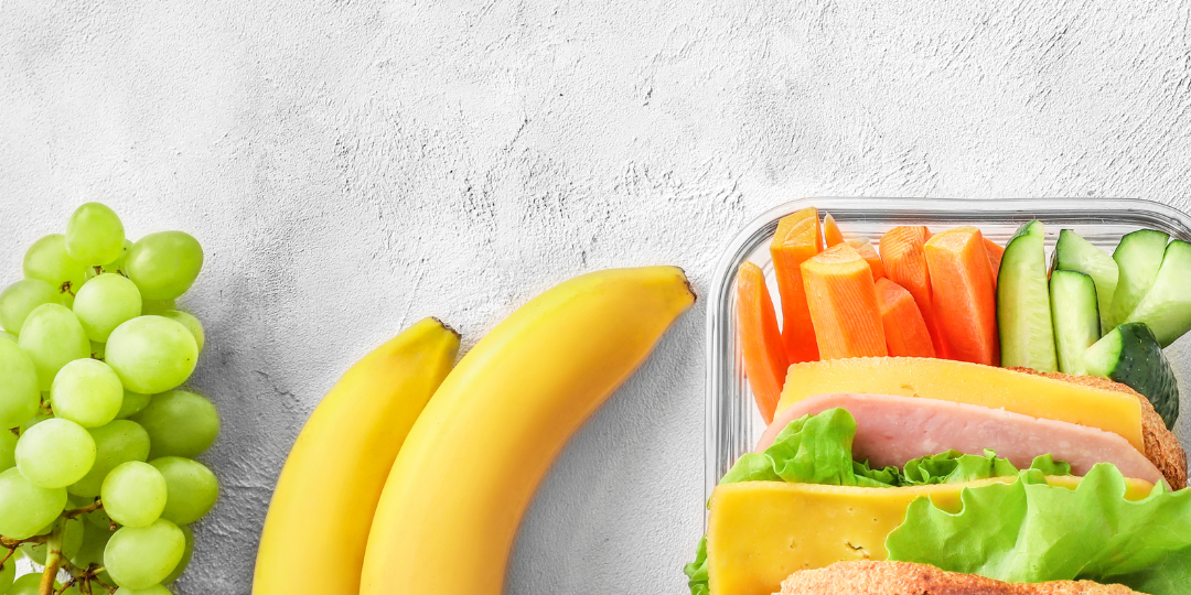A banana, green grapes, and a ham sandwich sit against a gray background A banana, green grapes, and a ham sandwich sit against a gray background