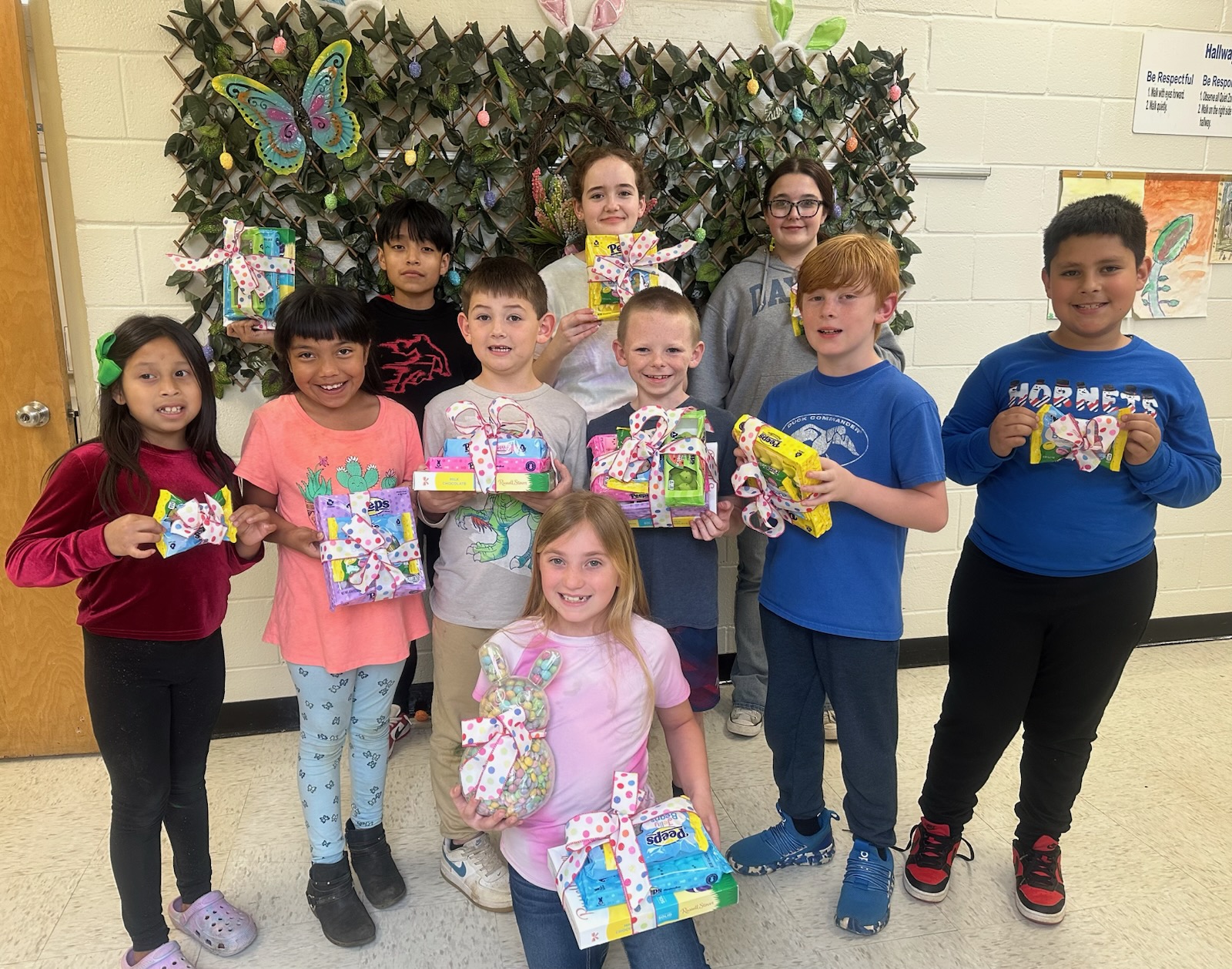 Photo of our Spring Contest Winners holding their prizes(Peeps, chocolate bunnies, ect.) standing in front of a spring decoration in the hallway. Back row:  Samuel Perez (6th grade), 1st place, middle school; Anzleigh Smith (6th grade), 2nd place, middle school; Bella Kerr (7th grade), 3rd place, middle school.  2nd row:  Hellen Marquez Vasquez (1st grade), 3rd place, Pre-K-2nd grade; Lucero Dominguez (2nd grade), 2nd place, Pre-K - 2; Winston Wood (1st grade), 1st place, Pre-K-2nd grade; Chance Hoover (4th grade), 1st place, 3rd-5th grade; Hudson Walker (3rd grade), 2nd place, 3rd-5th grade; Miguel Arreola (4th grade), 3rd place, 3rd-5th grade.   Bottom Row: Avery Moshier, 4th grade, Grand Prize Winner!