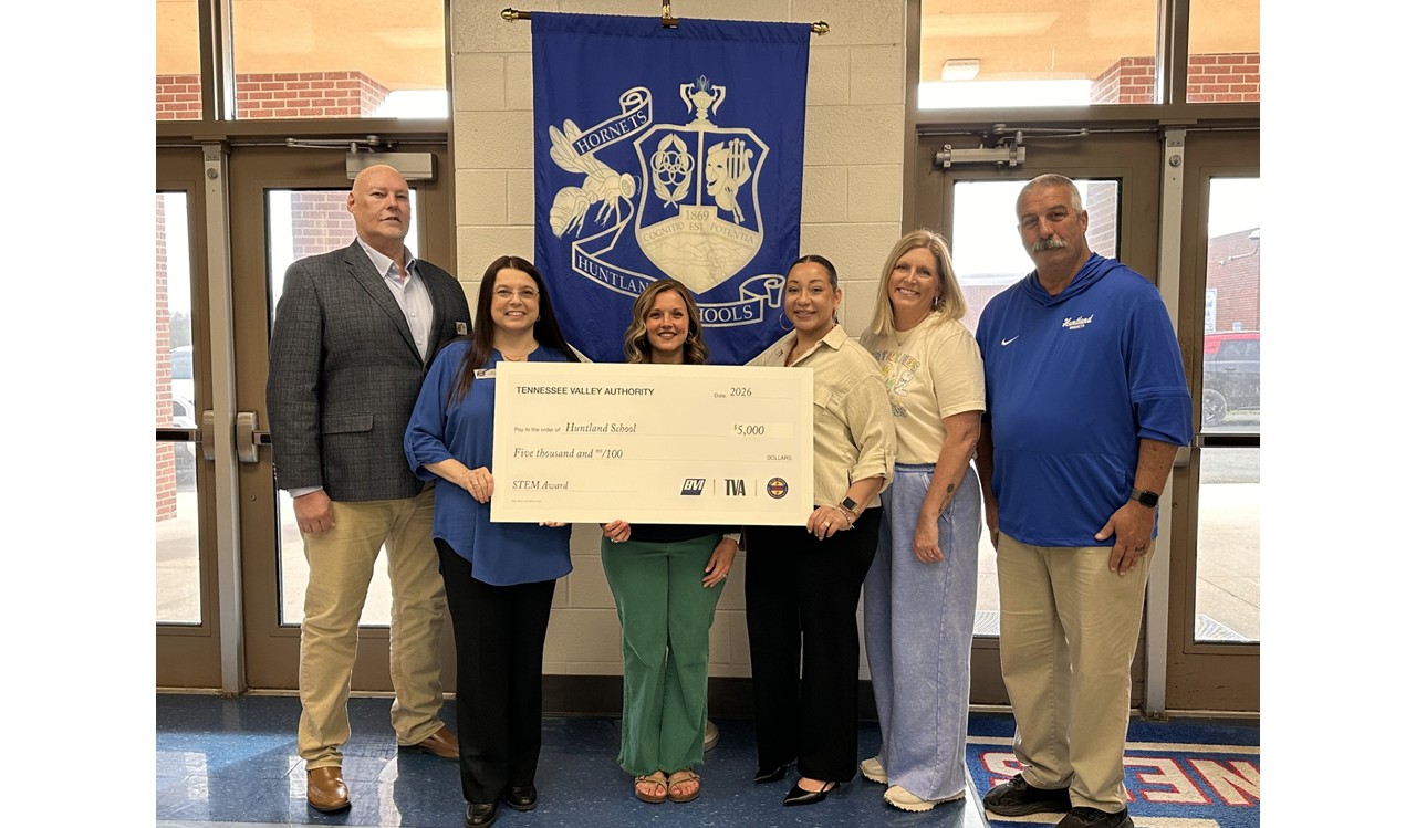 Photo of Grant being awarded to our Librarian Leslie Jones holding the $5,000 award from TVA. TVA staff and Huntland Assistant Principals Mrs. Sara Beth Spray and Mr. James Carr. Photo taken in the Huntland High School Lobby by the front door with the Huntland Banner/Flag behind them.